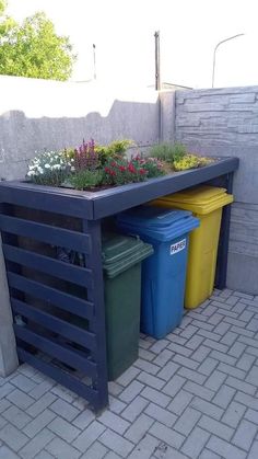 an outdoor planter with flowers and trash cans