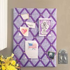 a purple bulletin board with pictures and magnets on it next to a vase filled with yellow flowers