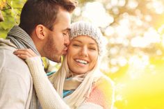 a man and woman kissing each other in front of trees with sunlight coming through the leaves