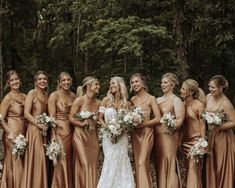 a group of women standing next to each other in front of trees and bushes with bouquets