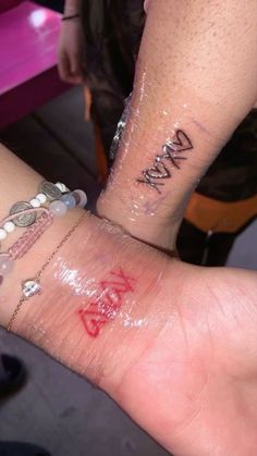 two people with tattoos on their arms holding each other's hands and one has writing on it