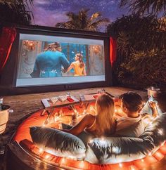 a man and woman sitting on a bean bag chair in front of a movie screen