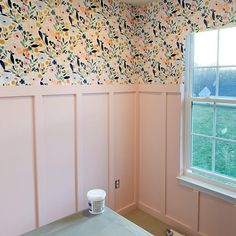 an empty room with pink walls and floral wallpaper on the walls, along with a bucket of paint