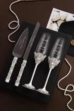 three wine glasses and two silverware in a black box with pearls on the table