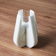 a white vase sitting on top of a wooden table next to a glass filled with water