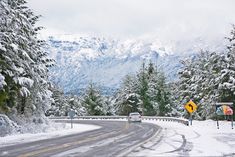 the road is covered in snow and has trees on both sides with mountains in the background