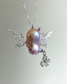 Elevate your elegance with this exquisite necklace that features a unique pendant designed to resemble an angel, featuring a lustrous baroque pearl. This stunning blend of natural beauty and exquisite craftsmanship floats with two large silver wings, with a dangling crystal butterfly and a twinkling star, providing a harmonious balance to the overall design. Whether you seek a distinctive touch for your evening attire or a fresh accent for your everyday jewelry, this piece is a perfect addition Silver Baroque Pearl Necklace Gift, Silver Baroque Necklace With Pearl Pendant, Baroque Silver Necklace With Pearl Pendant, Silver Baroque Pearl Jewelry, Baroque Silver Pearl Drop Necklace, Silver Baroque Jewelry Gift, Baroque Silver Jewelry Gift, Baroque Silver Jewelry As Gift, Silver Baroque Necklace With Pearl Charm