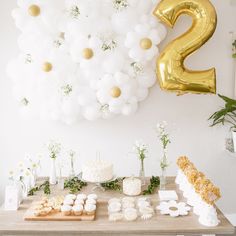 a table topped with lots of white and gold balloons next to a number two sign