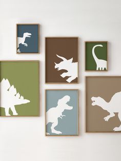 four framed dinosaur silhouettes are mounted on the wall in different colors and sizes, including green, blue, brown, and white