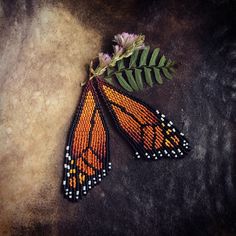 two orange and black beaded butterfly wings next to a flower on a stone surface