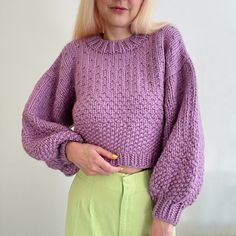 a woman with blonde hair wearing a purple sweater and green pants is standing in front of a white wall