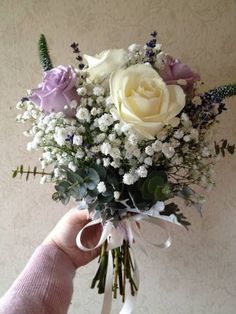 a person holding a bouquet of white and purple flowers with greenery in their hand