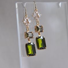 a pair of earrings with green and white stones hanging from it's earwires