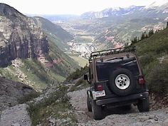 a jeep is parked on the side of a mountain trail with mountains in the background