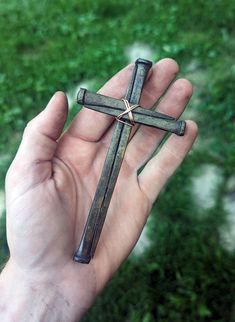 a hand holding a small cross in it's left palm, with grass in the background