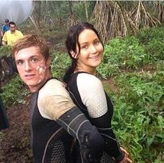 a man and woman with mud on their face standing in the woods, smiling at the camera