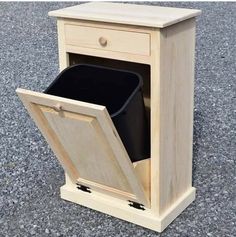 a wooden cabinet with a black trash can in the bottom drawer and one door open