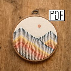 an embroidery project with mountains and sun in the background, on a wooden paneled surface