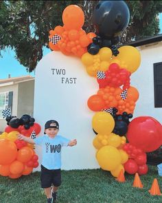 a young boy standing in front of a sign with balloons on it and the words two fast