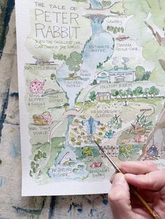 a person holding a paintbrush and drawing a map on paper with watercolors