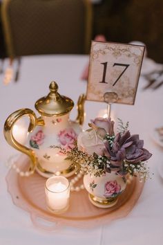 a tea pot with flowers and candles on a plate next to a candle holder that says 17