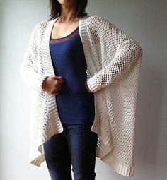 a woman standing in front of a wall wearing a white cardigan sweater and jeans