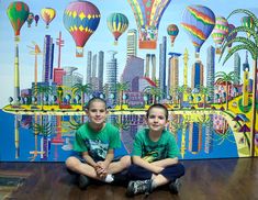 two young boys sitting on the floor in front of a colorful wall with hot air balloons