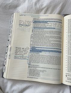 an open book sitting on top of a bed next to a white sheet with writing