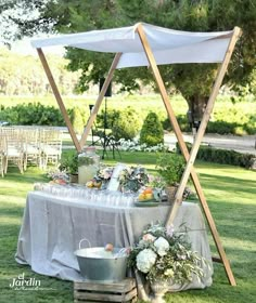 an outdoor table is set up with flowers and wine glasses on it, under a canopy