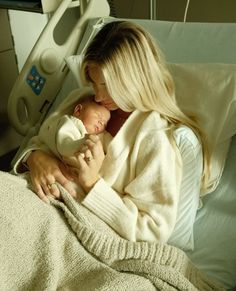 a woman holding a baby wrapped in a blanket on top of a hospital room bed