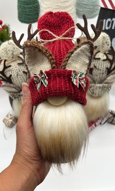 a hand is holding up a knitted reindeer head with antlers and bows on it