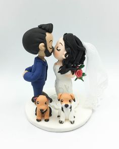 a wedding cake topper with two dogs and a bride kissing on the cheek, in front of a white background