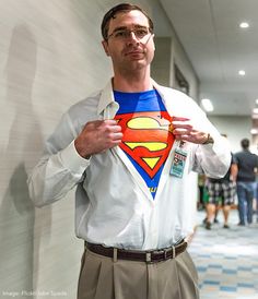 a man wearing a superman t - shirt and khaki pants stands in an office hallway