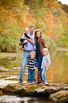 a family posing for a photo in front of a lake with fall leaves on the trees