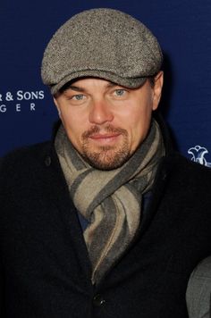 a man wearing a hat and scarf poses for a photo at an event in front of a blue background