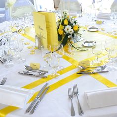 the table is set with yellow and white napkins, silverware, and flowers