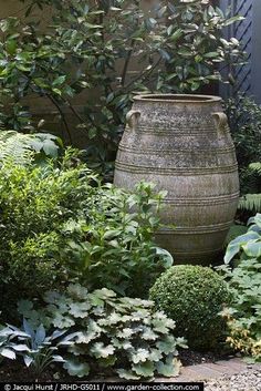 a large vase sitting in the middle of a garden surrounded by trees and bushes with text overlay