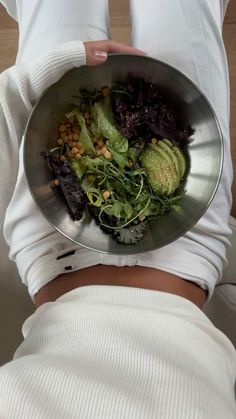 a woman is holding a metal bowl filled with vegetables and avocado on her stomach