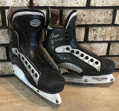 two black and white ice skates sitting against a brick wall