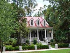 a small white house with red roof and pillars in the front yard, surrounded by trees