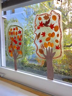 two paper trees in front of a window with fall leaves on the outside and inside