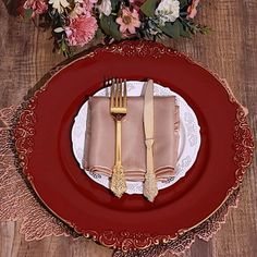 a red plate topped with a fork and knife next to a vase filled with flowers