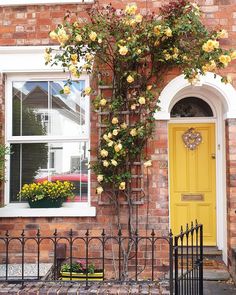 a yellow door and window on a brick building with flowers growing up the side of it