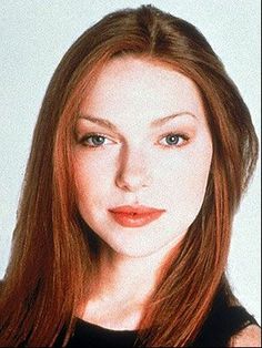 a woman with long red hair and blue eyes posing for a photo in front of a white background