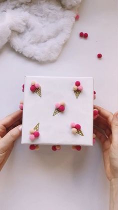 two hands are holding a white box with pink and gold ice cream cones on it