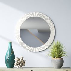 a round mirror on the wall next to a vase with a green plant in it