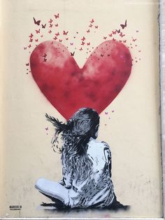 a woman sitting on the ground in front of a wall with a heart painted on it