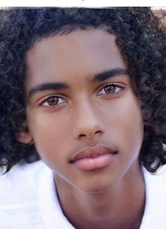 a close up of a person with curly hair wearing a white shirt and looking at the camera