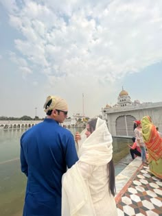 a man and woman standing next to each other near the water