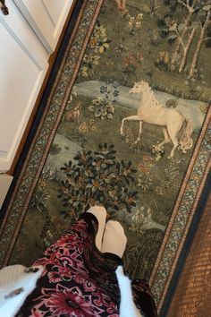 a person laying on the ground in front of a rug with a horse and forest scene